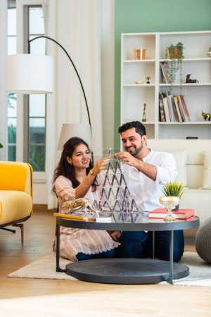 Photo for Indian asian young couple building a house using playing cards and having fun - Royalty Free Image