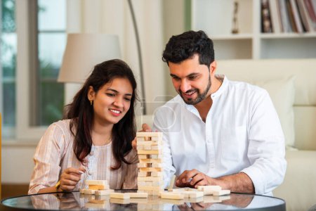 Photo for Indian young married couple playing jenga table game at home having fun - Royalty Free Image