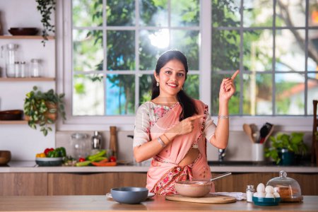 Téléchargez les photos : Attrayant indien asiatique jeune femme dans saree travail dans cuisine - en image libre de droit