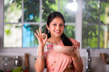 Téléchargez les photos : Attrayant indien asiatique jeune femme dans saree travail dans cuisine - en image libre de droit
