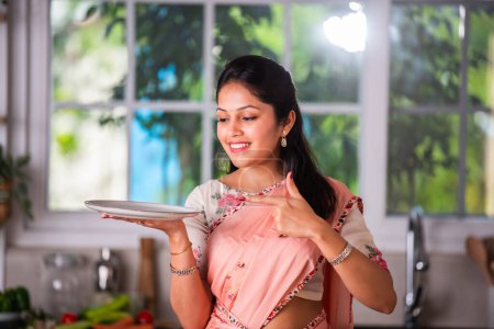 Foto de Atractiva india asiática joven hembra en saree trabajando en cocina - Imagen libre de derechos