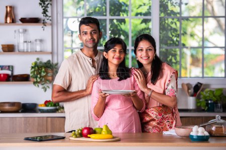Téléchargez les photos : Indien asiatique jeune couple avec fille enfant dans cuisine fabrication gâteau - en image libre de droit
