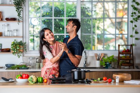 Cheerful millennial Indian asian husband and wife having fun and dancing in modern kitchen interior