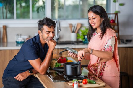 Photo for Indian asian couple preparing food at the stove with partner  in kitchen - Royalty Free Image