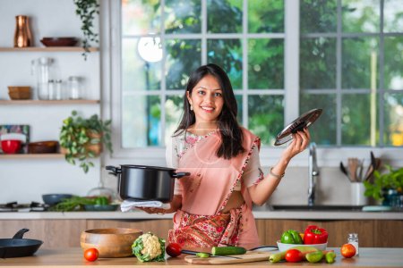 Photo for Indian asian young woman pointing, shocasing or promoting utensils, pot, spatula, empty plate, ok sign - Royalty Free Image