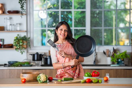 Photo for Indian asian young woman pointing, shocasing or promoting utensils, pot, spatula, empty plate, ok sign - Royalty Free Image