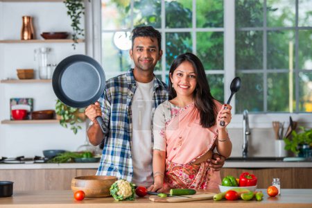 Foto de India asiático casado pareja en cocina promoción utensilios, vacío plato con ok signo - Imagen libre de derechos