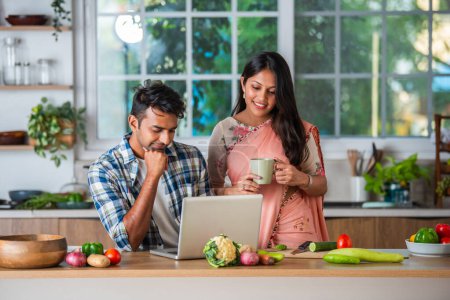Foto de India joven y atractiva pareja ocupada en la cocina usando ordenador portátil - Imagen libre de derechos