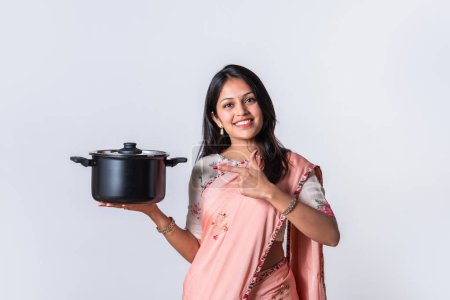 Photo for Indian pretty young woman in saree holding kitchen utensils standing isolated against white background - Royalty Free Image