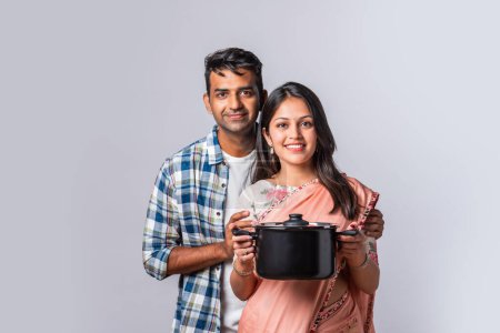 Téléchargez les photos : Portrait de sourire indien asiatique jeune couple avec des ustensiles de cuisine en bois et en métal, debout isolé sur blanc - en image libre de droit