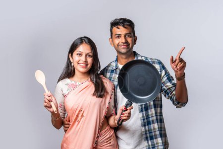 Foto de Retrato de la sonriente pareja joven asiática india con utensilios de cocina de madera y metal, de pie aislado en blanco - Imagen libre de derechos