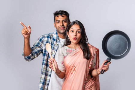 Photo for Portrait of smiling Indian asian young couple with wooden and metal kitchen utensils, standing isolated on white - Royalty Free Image