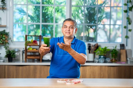 Foto de Indio asiático guapo mediana edad hombre beber saludable verde bebida o smoothie en cocina - Imagen libre de derechos