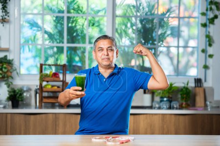 Téléchargez les photos : Indien asiatique beau moyen âge l'homme boire sain vert boisson ou smoothie dans cuisine - en image libre de droit