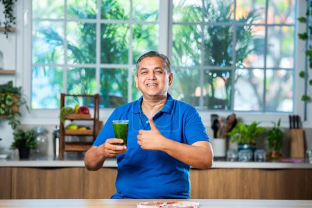 Photo for Indian asian Handsome mid age man man drinking healthy green drink or smoothie in kitchen - Royalty Free Image