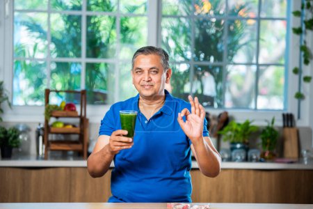 Foto de Indio asiático guapo mediana edad hombre beber saludable verde bebida o smoothie en cocina - Imagen libre de derechos