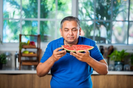 Photo for Indian asian mid age man enjoy eating watermelon fruit over white or kitchen background - Royalty Free Image