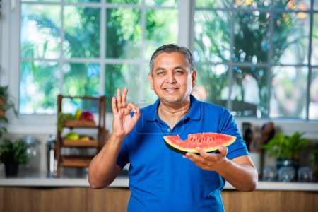 Photo for Indian asian mid age man enjoy eating watermelon fruit over white or kitchen background - Royalty Free Image