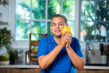 Téléchargez les photos : Indien asiatique heureux moyen âge l'homme holding ou montrant mûr mangue fruit - en image libre de droit