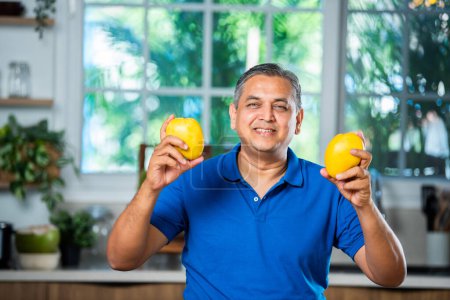 Indischer asiatischer glücklicher Mann mittleren Alters, der reife Mango-Früchte hält oder zeigt