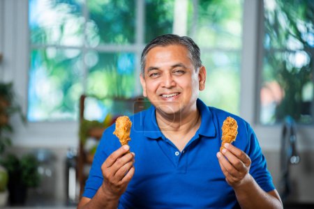 Asian indian mid age man eating fried chicken leg piece