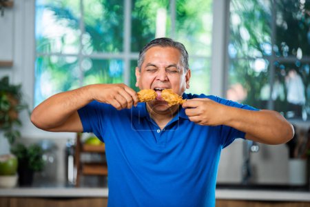 Asian indian mid age man eating fried chicken leg piece
