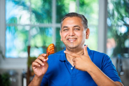 Téléchargez les photos : Asiatique indien moyen âge homme manger frit poulet jambe morceau - en image libre de droit