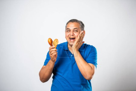 Téléchargez les photos : Asiatique indien moyen âge homme manger frit poulet jambe morceau - en image libre de droit