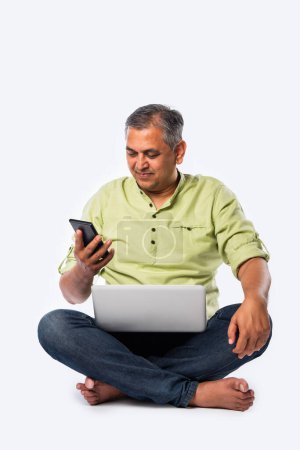 Téléchargez les photos : Moyen âge indien asiatique bel homme en utilisant ordinateur portable, debout ou assis sur fond blanc - en image libre de droit