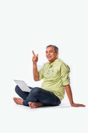 Téléchargez les photos : Moyen âge indien asiatique bel homme en utilisant ordinateur portable, debout ou assis sur fond blanc - en image libre de droit