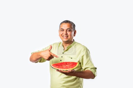 Foto de Indio asiático mediana edad hombre disfrutar comer sandía fruta sobre blanco o cocina fondo - Imagen libre de derechos
