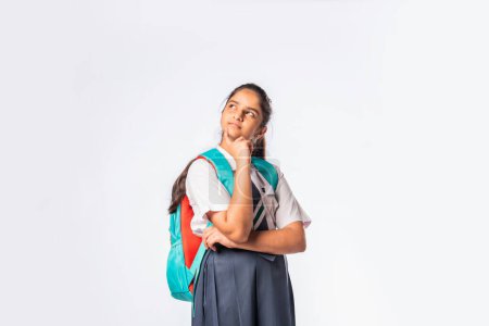 Téléchargez les photos : Indien asiatique expressif adolescent écolière avec uniforme et sac à dos debout isolé contre blanc - en image libre de droit