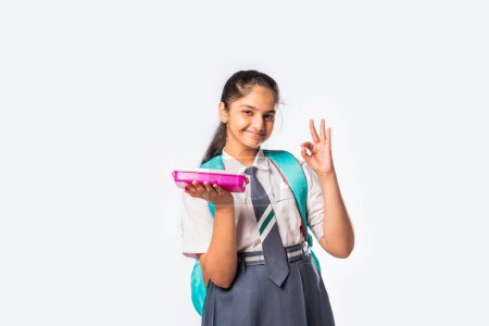 Foto de Feliz indio asiático colegiala en la escuela uniforme celebración un almuerzo caja sobre blanco fondo - Imagen libre de derechos
