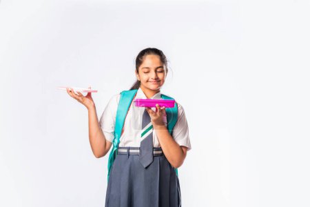 Photo for Happy Indian asian schoolgirl in school uniform holding a lunch box against white background - Royalty Free Image