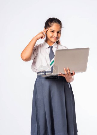 Photo for Small Indian asian schoolgirl working on laptop computer while standing isolated against white background - Royalty Free Image