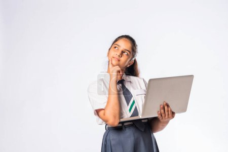 Téléchargez les photos : Petite écolière asiatique indienne travaillant sur ordinateur portable tout en restant isolée sur fond blanc - en image libre de droit