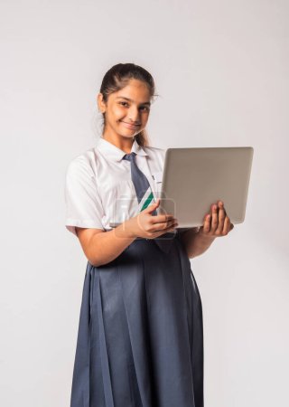 Photo for Small Indian asian schoolgirl working on laptop computer while standing isolated against white background - Royalty Free Image
