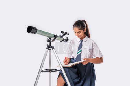 Téléchargez les photos : Petite écolière indienne asiatique en uniforme scolaire avec télescope sur fond blanc - en image libre de droit
