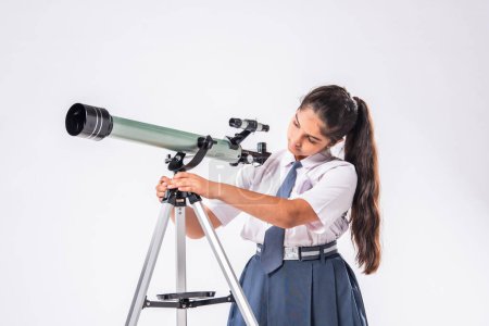 Foto de Pequeña colegiala asiática india en uniforme escolar con telescopio sobre fondo blanco - Imagen libre de derechos