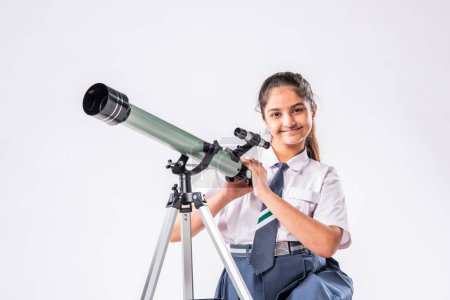 Photo for Little Indian asian schoolgirl in school uniform with telescope on white background - Royalty Free Image