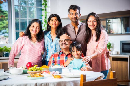 Photo for Portrait of Indian family of three generations eating meals together at home looking at camera - Royalty Free Image