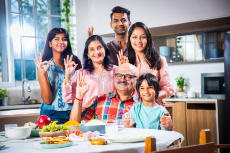 Photo for Portrait of Indian family of three generations eating meals together at home looking at camera - Royalty Free Image