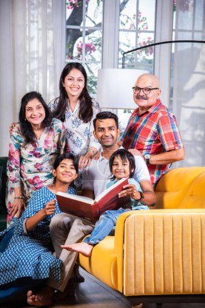 Photo for Indian asian multigenerational family watching photos in album or reading book while sitting on sofa together - Royalty Free Image