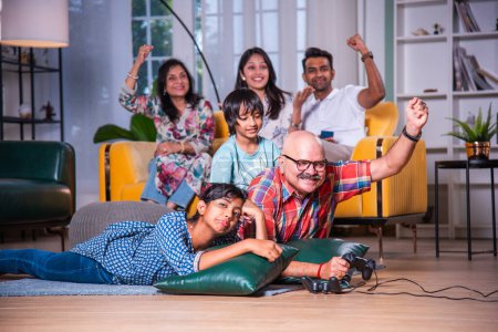 Photo for Indian asian grandpa playing video game with grandchildren lying on floor at home - Royalty Free Image