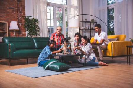 Téléchargez les photos : Indien asiatique multigenerational famille joue en bois bloc empilage jeu à la maison ensemble et avoir amusant - en image libre de droit