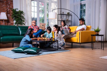 Photo for Joyful Indian asian kids playing chess in living room with senior grandparents and parents at home - Royalty Free Image