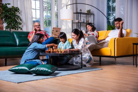 Téléchargez les photos : Joyeux indien asiatique enfants jouer aux échecs dans le salon avec les grands-parents seniors et les parents à la maison - en image libre de droit