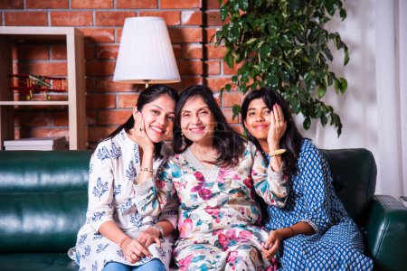 Photo for Portrait of happy Indian asian three generations of females, grandma, daughter and grand daughter sitting on sofa - Royalty Free Image
