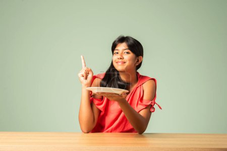 Photo for Indian asian adorable teenage girl holding empty plate and pointing or advertising something - Royalty Free Image