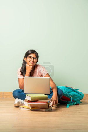 Photo for Indian asian school girl in casual wear using laptop for study sitting on floor isolated - Royalty Free Image